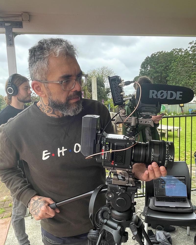 Jared Flitcroft adjusts the lens of a cinema camera on a tripod during filming.