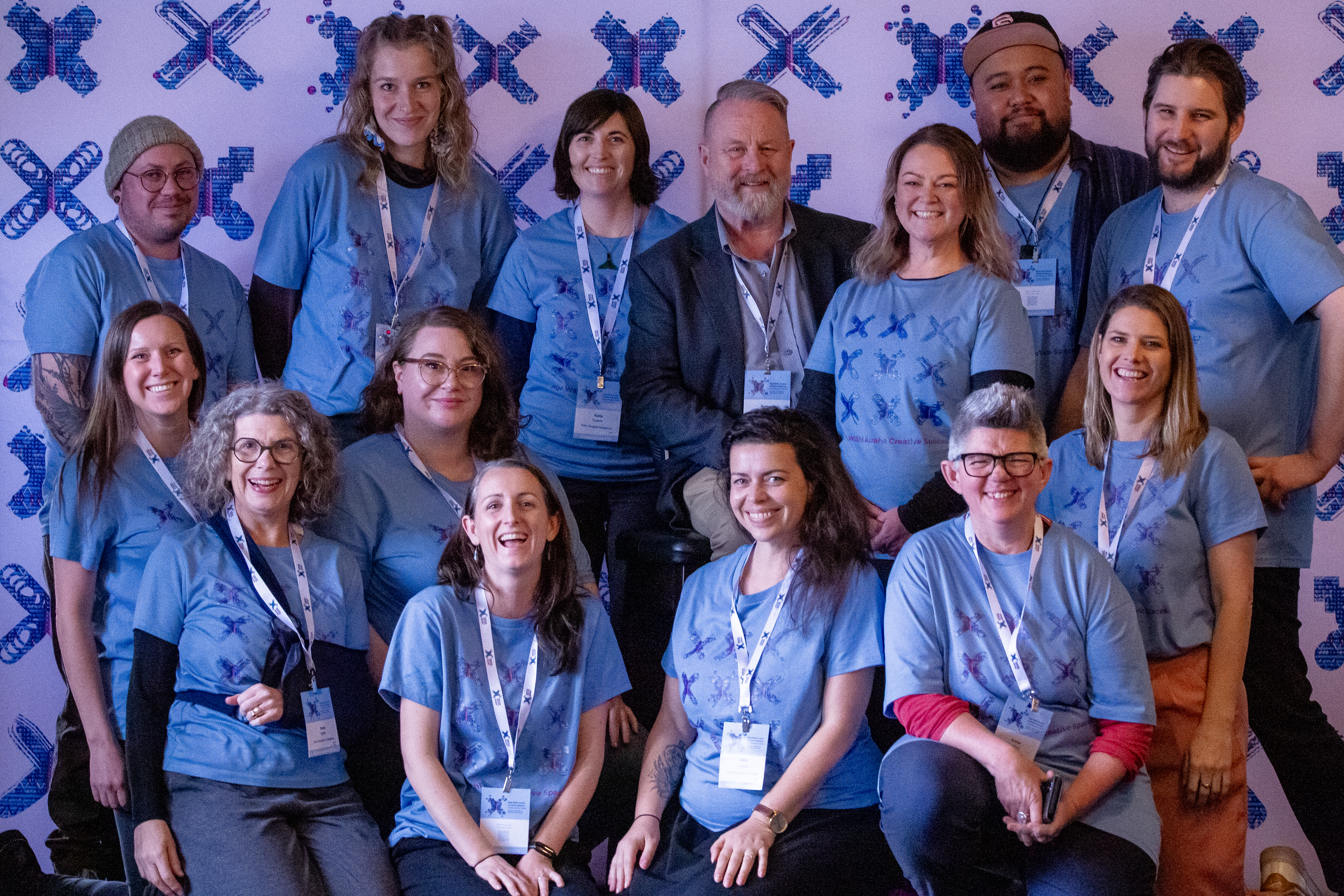 A group of Arts Access Aotearoa staff at Ngā Wāhi Auaha Creative Spaces Conference 2024, wearing blue tee-shirts designed for the conference