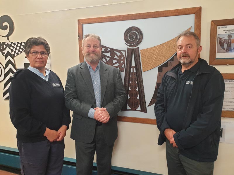 Leonie Aben, Richard Benge and Tony Abbott stand in front of artwork at Hawke's Bay Regional Prison in 2021