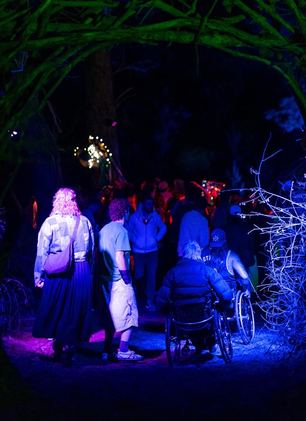 Festival-goers move through a forest path at night toward a stage with a dimly-lit crowd in the background Photo: Lucas Perelini