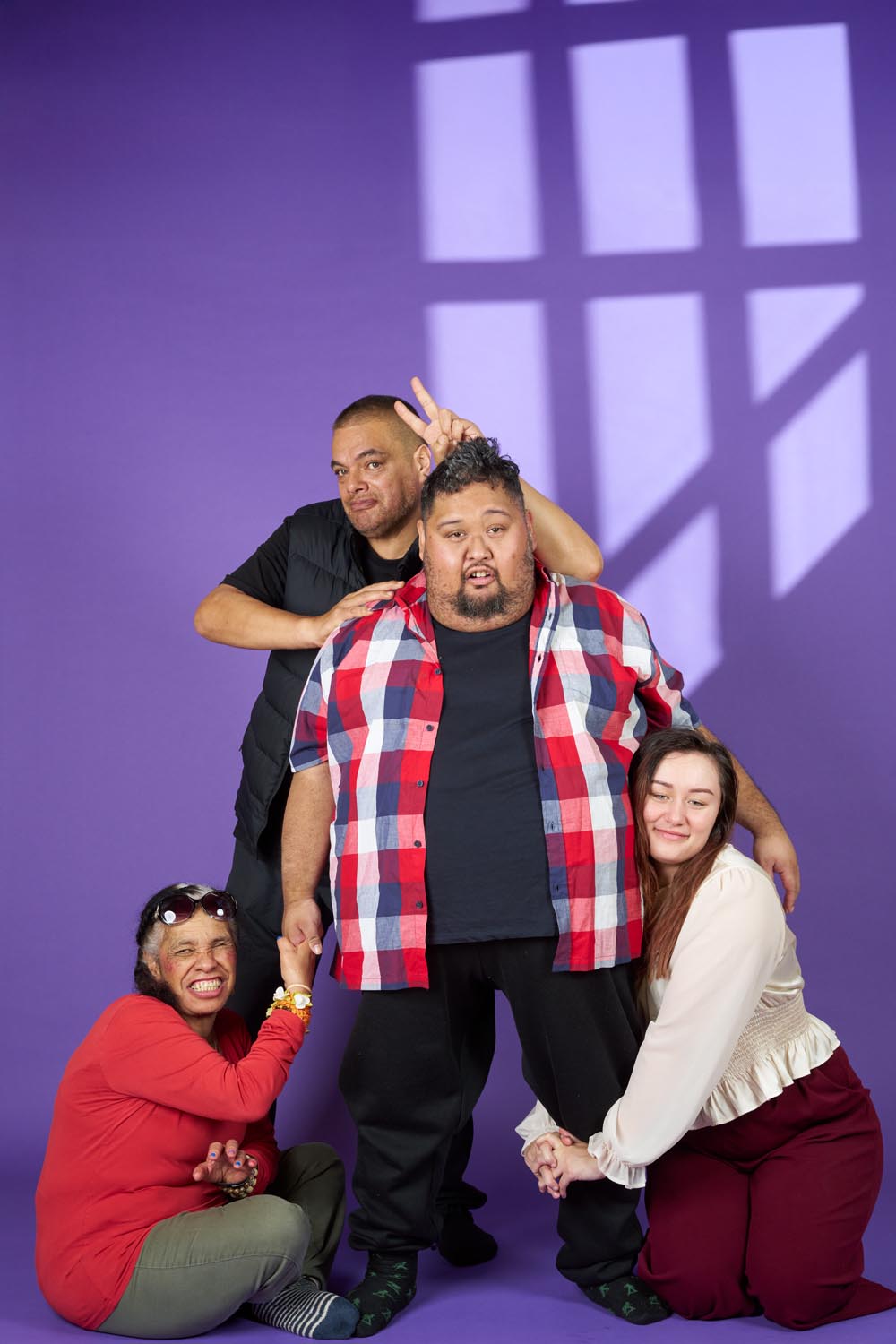 The Siblings cast against a purple background. Jordan is standing looking confused, Roka is sitting, smiling and grabbing his hand while Kiriana kneels holding his other leg. Dazz is standing behind Jordan doing a peace sign above his head. 