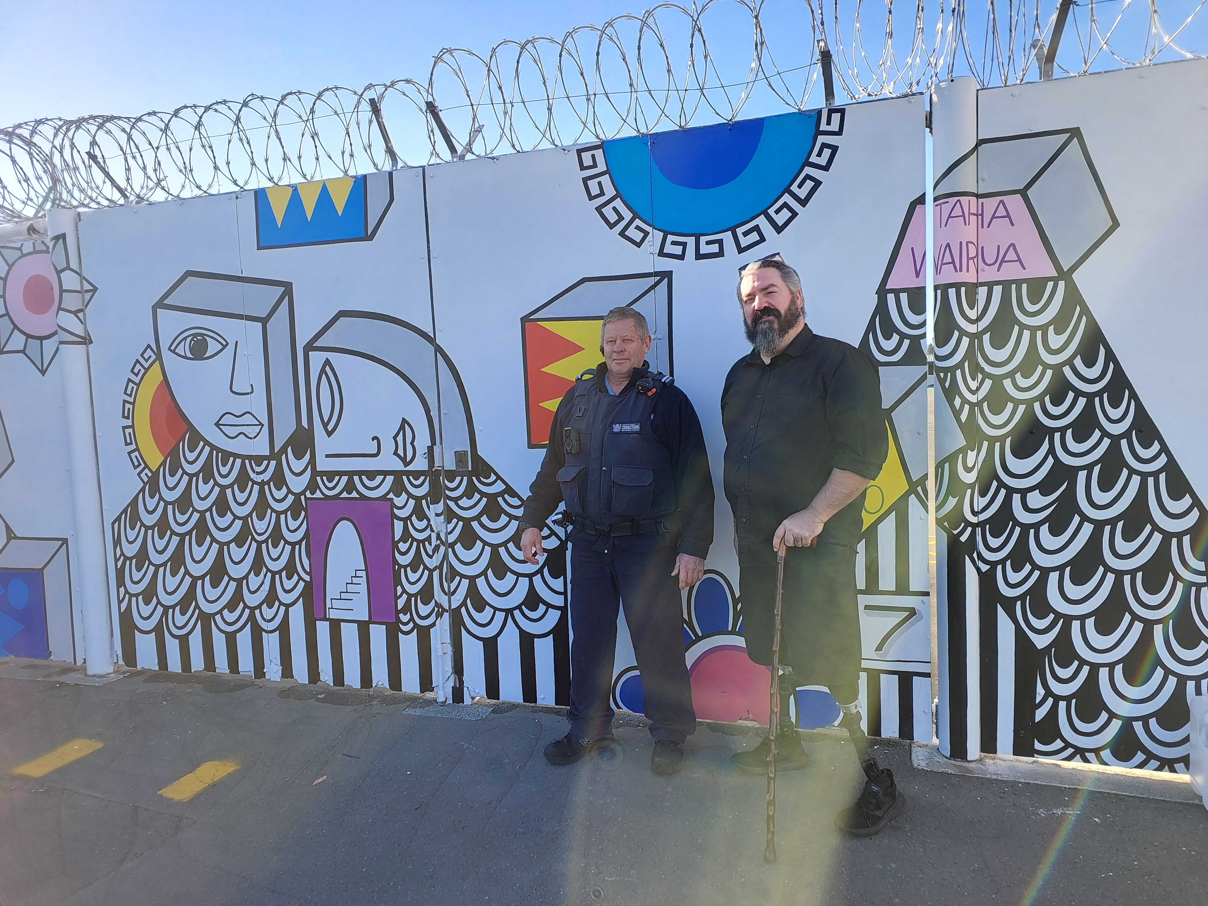 Neil Wallace stands in front of a colourful mural painting on the inside of the prison wall at Hawkes Bay Regional Prison.