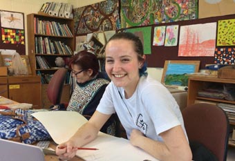 Arts for Health attendee smiling broadly at the camera while working on her art